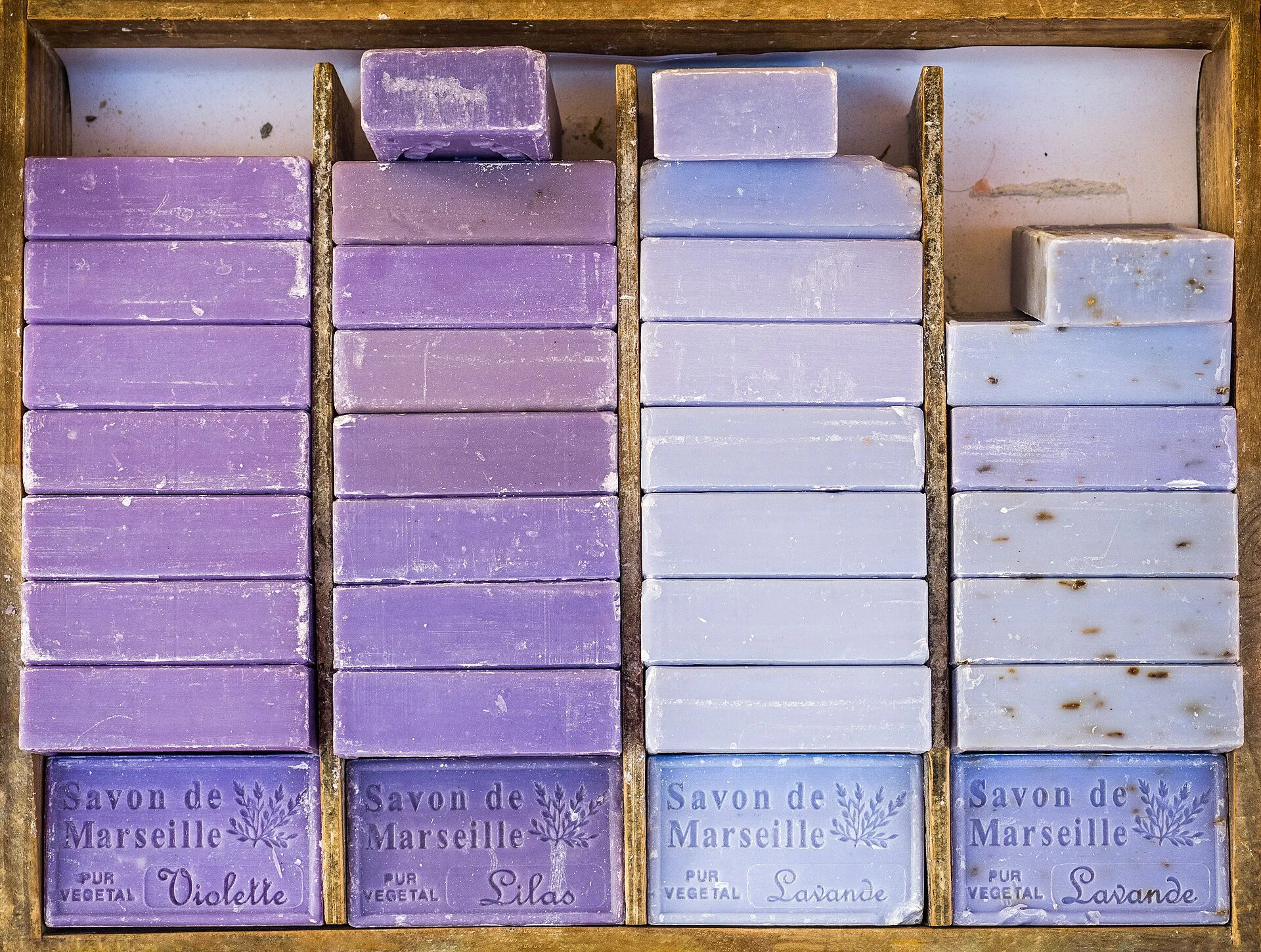 Gestapelte Seifenstücke in Violett- und Lavendeltönen im Holzregal