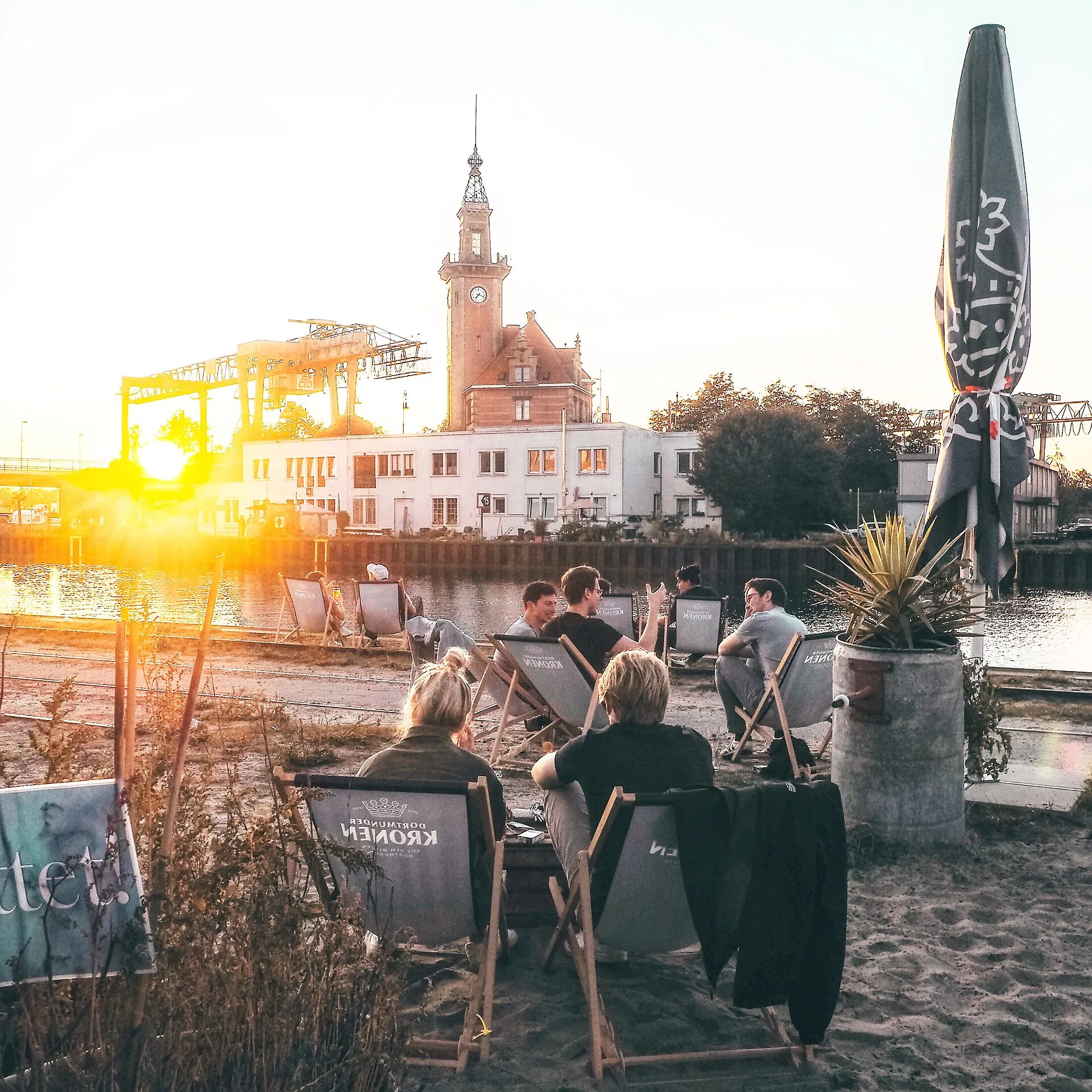 Liegestühle im Sand am Dortmunder Hafenbecken bei Sonnenuntergang