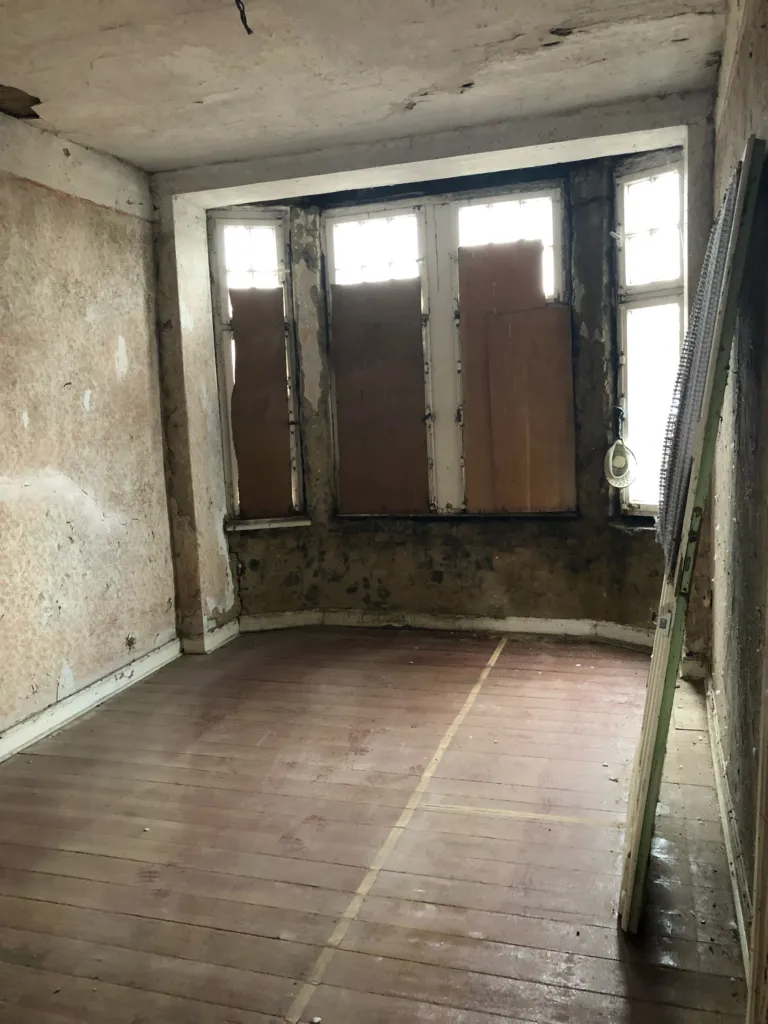 Vacant room with a bay window, closed wooden shutters and old floorboards