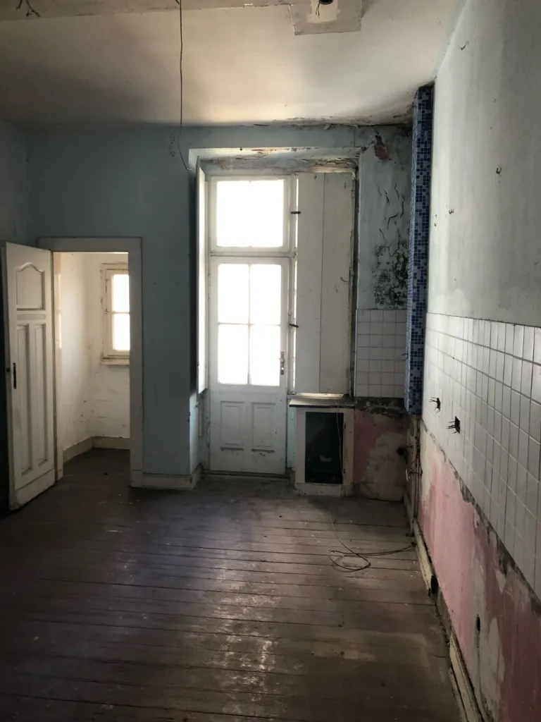 Abandoned kitchen with remnants of tiles and a balcony door